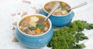 "Heerlijke huisgemaakte soep met vleesballetjes, groenten en verse kruiden, geserveerd in blauwe keramieken kommen op een decoratief tafelkleed.
